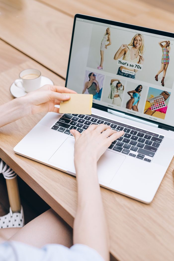 Des mains tenant une carte de crédit pendant des achats en ligne sur un ordinateur portable posé sur une table en bois.